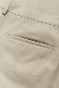 Bež hlače z gladko, mehko teksturo imajo en sam zadnji žep s pasico. Čisti šivi in krojen pas.