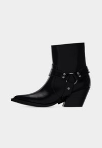 Svart ankelstövel med spetsig tå, slät lackläderfinish, lagrad rem med spänne och metallbeslag samt klack med staplad design.