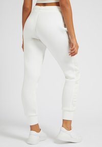 Weiße Jogginghosen mit tailliertem Design, gerippten Bündchen und glatter Textur. Seitenstreifen sorgen für Details. Kombiniert mit weißen Sneakers.