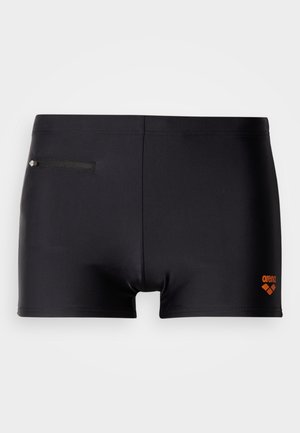 Svarte badeshorts laget av glatt stoff, med en oransje logo og en liten glidelåslomme på baksiden for oppbevaring.