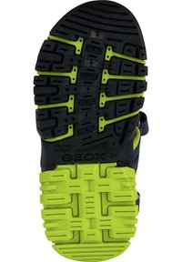 Black rubber shoe sole with green accents. Features deep tread, ventilation holes, and embossed branding. Designed for grip and breathability.