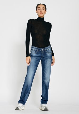 Schwarz langärmliges Oberteil mit Rollkragen, kombiniert mit blauen geraden Jeans. Die Jeans verfügen über fünf Taschen, Gürtelschlaufen und einen dezenten Ausblass.