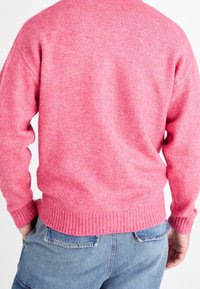 Różowy sweter z dzianiny z prążkowanym dołem i mankietami, o gładkiej fakturze i prostym kroju. Stylizowany z jasnoniebieskimi spodniami dżinsowymi.