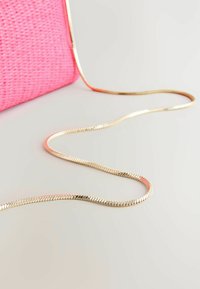 Vaaleanpunainen kudottu clutch-laukku, jossa on metallinen kultaketjusankka. Sankka on litteä ja sileä, mikä kontrastoi laukun teksturoitua pintaa.