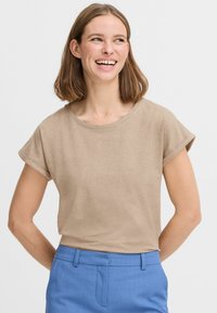 Maglietta beige a maniche corte con scollatura tonda, morbido al tatto, indossata dentro dei pantaloni azzurri chiari, con maniche arrotolate.
