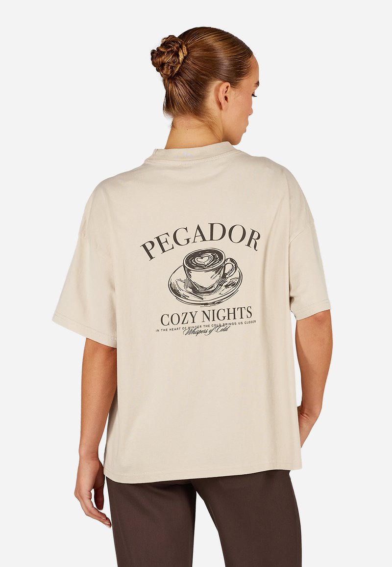 Beige liela izmēra t-krekls, izgatavots no kokvilnas, ar grafisko dizainu, kurā attēlots kafijas krūze un uzraksts aizmugurē. Īsas piedurknes, brīvs piegriezums.