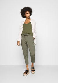 Olive green tank top layered with a light beige button-up shirt, paired with olive jogger pants and black platform sandals.