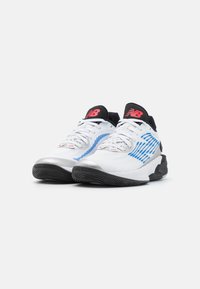 White athletic shoes with blue stripes and a silver toe cap. Features a black and red logo on the tongue, textured sole, and laces.