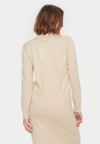 Långärmad beige stickad klänning med ribbat krage, normal passform, mjuk textur och diskret melerat mönster. Banden vid ärmsluten och fållen.