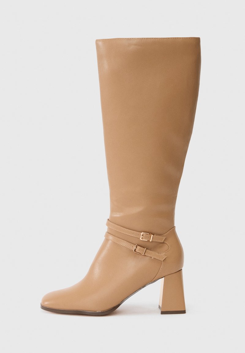 Botte en cuir beige arrivant au genou avec un bout arrondi, un talon carré et deux sangles ajustables avec des boucles en métal. Texture lisse et design minimal.