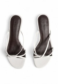 White strappy sandals with a flat design, featuring a brown leather insole and minimalistic straps. Smooth texture with no visible patterns.