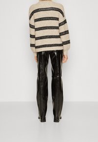 Randig stickad beige tröja med svarta ränder, i kombination med högblanka svarta skinnbyxor. Tröjan har en avslappnad passform och ribbat mönster.