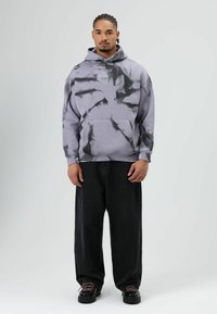 Lichtgrijze hoodie met zwarte tie-dye patronen, kangoeroezak, geribbelde manchetten, gecombineerd met losse zwarte denim jeans en zwarte platform schoenen.