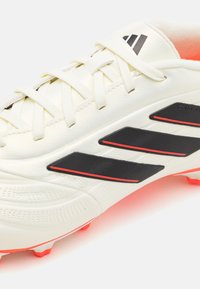 Scarpino da calcio bianco con materiale texturizzato, strisce nere e accenti rossi. Presenta lacci e tacchetti moldati per una migliore trazione.