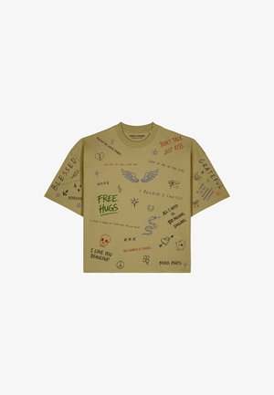Maglietta a maniche corte color cammello con scarabocchi e frasi in stile scritto a mano come "FREE HUGS," ali, un teschio, serpente e "DON'T TALK JUST KISS."