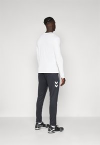 Valge pika varrukaga särk, mis on kombineeritud tumesiniste sportpükstega, millel on valged chevroni triibud. Mustad spordijalanõud logoga.