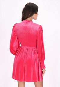 Rochie din catifea roz, cu spate plisat, mâneci lungi bufante, guler cu volane și fustă clopot care se strânge în talie.