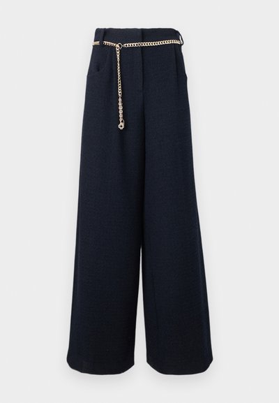 Παντελόνια με φαρδιά μπατζάκια σε μαύρο χρώμα, με πλαϊνές τσέπες και λεπτή χρυσή ζώνη αλυσίδα με ένα μικρό φυτικό γούρι.