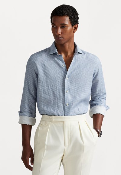 Chemise à motifs bleu clair avec un col classique et un devant boutonné, associée à un pantalon taille haute de couleur crème avec des boutons doubles.