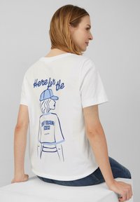 T-shirt en coton blanc avec une illustration graphique bleue d'une personne portant une casquette, avec le texte "Ici pour les bons moments uniquement" au dos.
