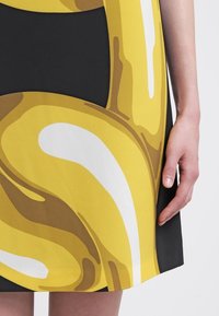Gros plan sur une jupe noire avec un motif abstrait jaune, blanc et marron audacieux et une main reposant sur le côté.