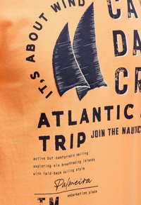 Orange cotton T-shirt with a navy graphic featuring two sailboat sails and text, including "Atlantic Trip" and "Palmeira."