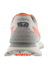 Zapatilla gris con acentos naranjas, tejido texturizado y ante liso. Presenta un logo en la parte trasera y "MCMLXXXV" grabado en la entresuela.
