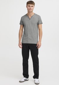 Camiseta gris de manga corta y escote en V con tres botones decorativos, combinada con pantalones negros y zapatillas blancas con rayas negras. Diseño sencillo y casual.