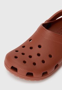 Brown clog made of synthetic material, featuring ventilation holes, a textured surface, and a back strap for secure fit.