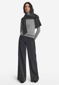 Grå långärmad topp i kombination med vida mörkblå jeans, kompletterad med en strukturerad svart scarf draperad över axlarna.