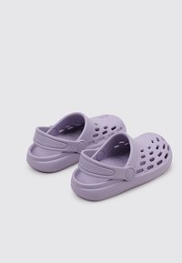 Une paire de sabots légers violets avec des trous de ventilation et des sangles de talon réglables, posée sur un fond gris clair uni.