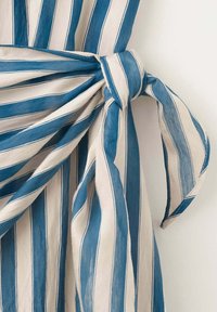Tissu rayé verticalement bleu et blanc, noué en un nœud souple avec des extrémités lâches sur un fond clair uni.