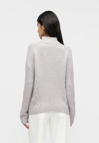 Ανοιχτό γκρι πλεκτό πουλόβερ με ψηλό γιακά, με ριμπάτο τελείωμα και σχέδιο πλεξούδα στα μανίκια. Μαλακή υφή, άνετη εφαρμογή.