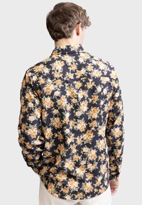Langarmhemd aus dunklem Stoff mit einem weißen und orangefarbenen Blumenmuster, klassischem Kragen und Knopfdetail im Rücken.
