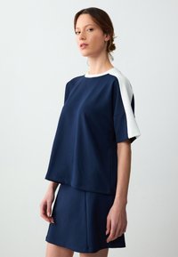 Top blu navy, dal taglio morbido, con accenti di pannello bianco e maniche corte. Abbinato a una gonna blu navy coordinata, entrambi realizzati in tessuto morbido.