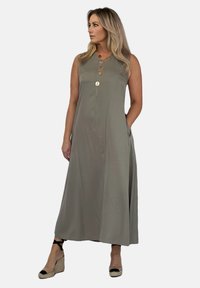 Khaki sansrękawowa sukienka maxi z okrągłym dekoltem, detalami kieszeni i złotym guzikiem jako akcentem. Noszona z espadrylami na koturnie. Gładka tekstura.