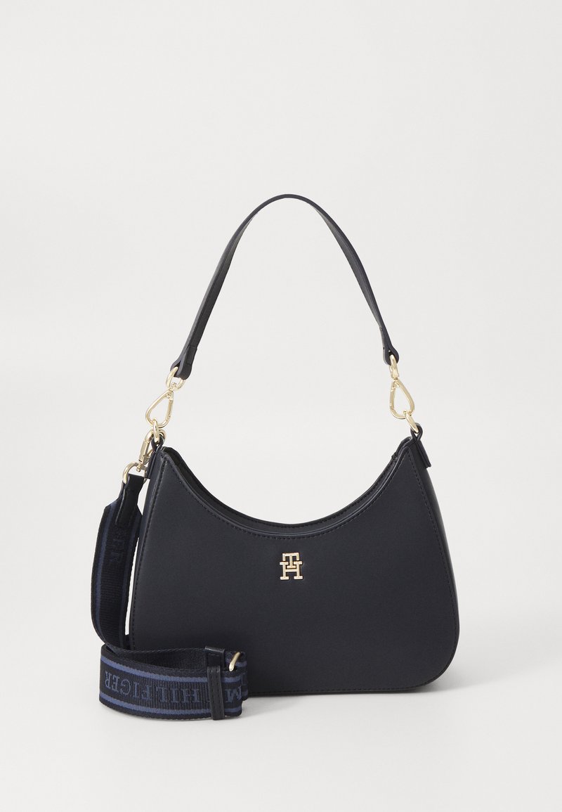 Marine leren handtas met een gebogen silhouet, gouden logo accent en een afneembare schouderband met een blauw tekstpatroon. Glad oppervlak.