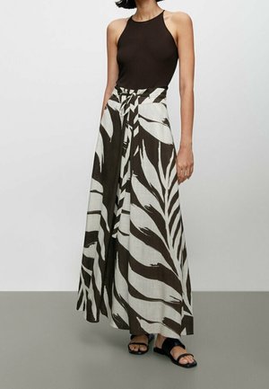 Débardeur marron associé à une longue jupe maxi beige à motifs avec des feuilles brun foncé ; modèle portant des sandales plates noires.