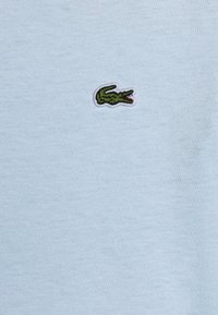T-shirt di cotone azzurro chiaro con un piccolo logo di coccodrillo verde ricamato sul petto. Tessuto morbido con una finitura liscia.