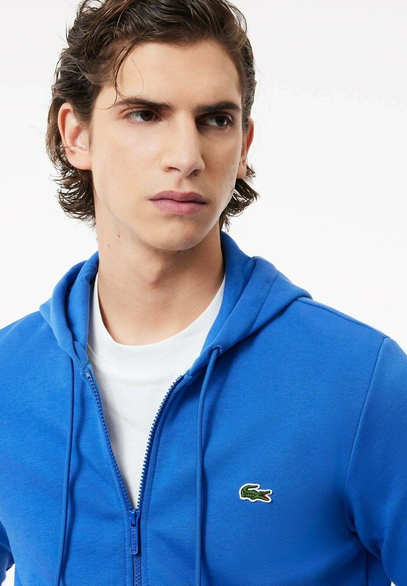 Felpa con zip blu realizzata in misto cotone, con interno bianco, tasca a marsupio e un piccolo logo ricamato di un coccodrillo sul lato sinistro del petto.