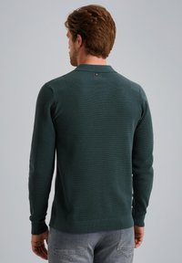 Suéter de punto verde oscuro con mangas largas, cuello tipo polo y puños acanalados. La parte posterior tiene un pequeño detalle de logo en el cuello.