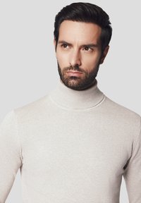 Beżowy sweter z golfem wykonany z prążkowanej dzianiny, z wysokim kołnierzem i dopasowanym krojem, prezentujący gładką teksturę i prosty styl.