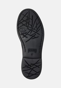 Semelle de chaussure en caoutchouc noir avec un motif de semelle en croix abstrait, logo de la marque "Camper" et marquage de taille 42 sur un fond blanc.