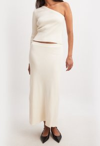 Cremfarbener, gerippter Zweiteiler mit einem Schultertop und einem langen, körperbetonten Rock. Das Top hat ein kurzes Design und beide Teile sind glatt.