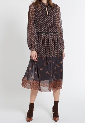 Robe noire en tissu transparent avec des manches longues, présentant un décolleté en forme de trou de serrure et un motif de feuilles brunes et d'ovales sur l'ensemble. Longueur mi-mollet.