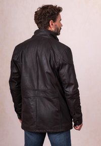 Brown leather jacket with a high collar, structured seams, and buttoned cuffs. Features a smooth texture and a regular fit.