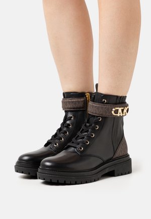 Bottes cheville en cuir noir avec une sangle marron texturée, un matériel doré et une semelle en caoutchouc résistante ; avec fermeture à lacets à l'avant et fermeture éclair latérale.