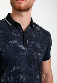 Námořnická polo košile s květinovým vzorem, Texturovaná látka, černý límec s bílými akcenty, zapínání na dva knoflíky a vyšívané logo.