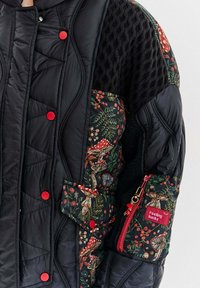 Czarna pikowana kurtka z kwiatowym i grzybowym wzorem na jednym rękawie, czerwonymi zatrzaskami oraz małą kieszonką na zamek z metką.