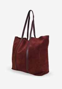 Bolso tote de ante en burdeos oscuro con dos asas largas de cuero. Presenta un diseño simple y una textura suave, ideal para uso casual.